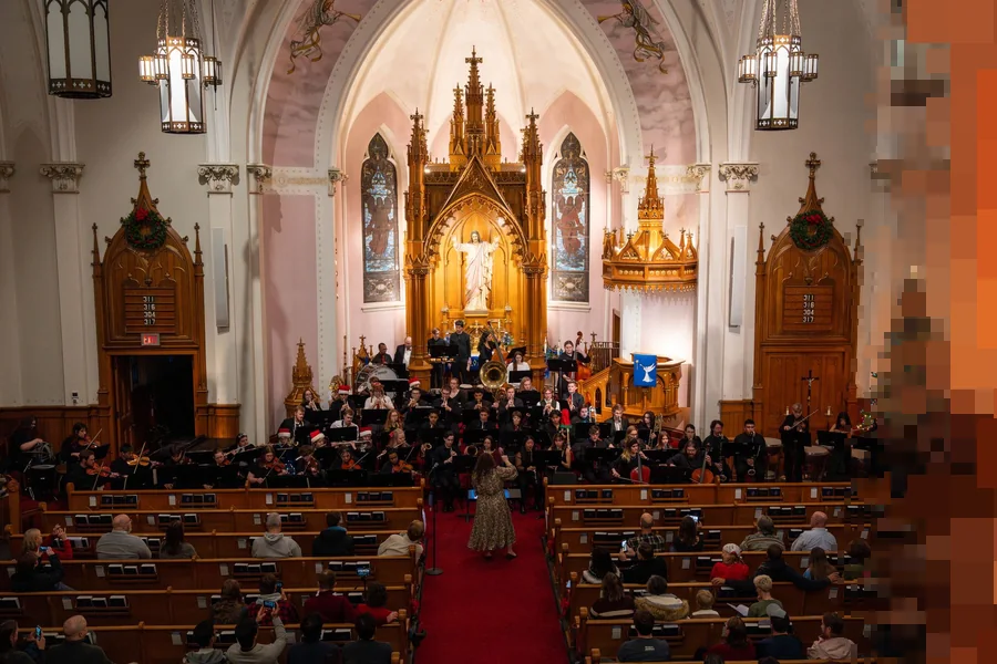 Et orkester spiller julekonsert foran et forgylt alter i en kirke med fullsatte benker