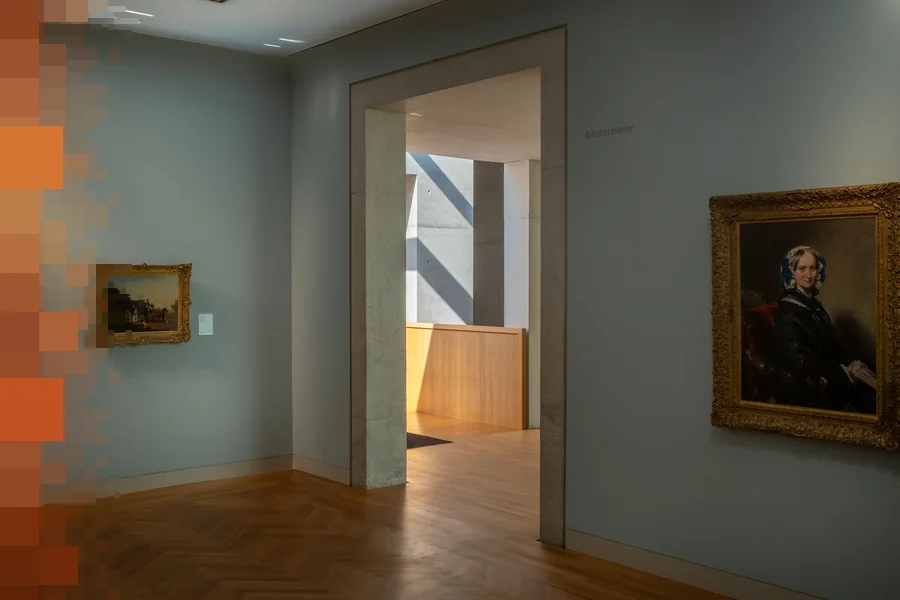 Et stille museumsrom med lyseblå vegger, parkettgulv og gamle malerier i gullrammer, med en åpen døråpning inn til neste sal