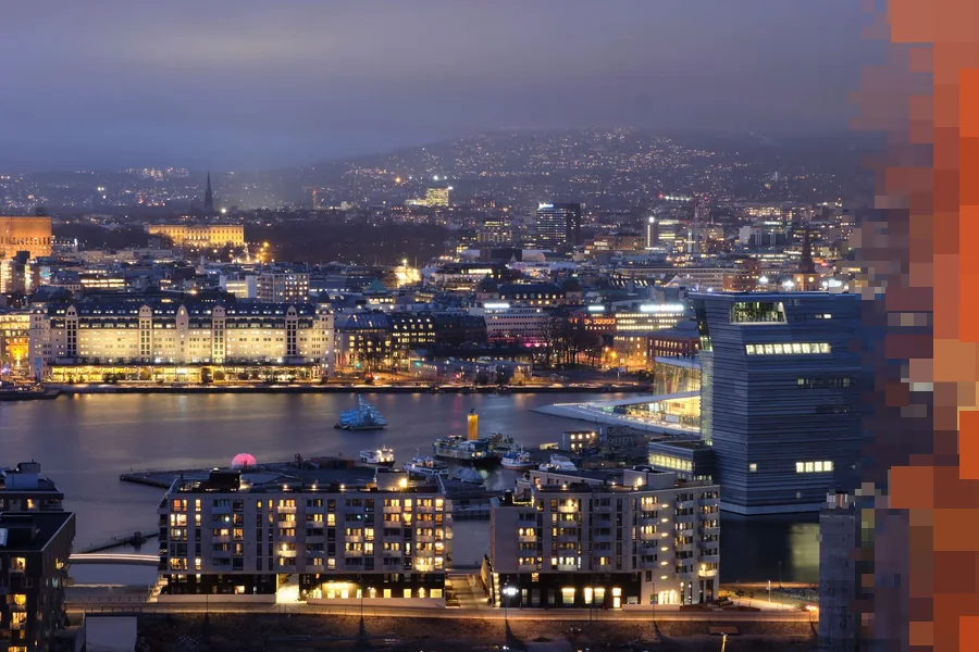 Oslo sentrum i blåtimen sett ovenfra, med lys i husene langs havnen og åsene bak byen
